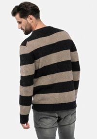 Gestreifter Pullover in Schwarz und Beige mit strukturiertem Muster und gerippten Bündchen, kombiniert mit grauen Hosen. Rückansicht dargestellt.