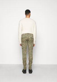 Gröna kamouflage cargobyxor med flera sidofickor; kombinerade med en vit stickad tröja och svarta stövlar, sedd bakifrån.