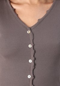 Brown ribbed top with a V-neck and scalloped edges; features five cream-colored buttons down the front for closure.