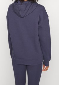 Mörkblå hoodie i mjukt tyg, med snörning i huvan, sänkt axlar och ribbade manschetter och nederkant för en avslappnad passform.
