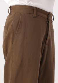 Brown trousers made of textured fabric, featuring a flat front, belt loops, and a zipper closure on the side.