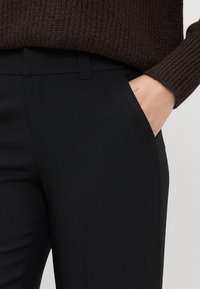 Black tailored pants with a smooth texture, featuring side pockets and a clean waistband, paired with a brown ribbed sweater.