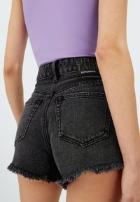 Donkergrijze denimshorts met een rafelige zoom, voorzien van twee achterzakken en een merketiket op de tailleband. Glad textuur, aansluitend ontwerp.