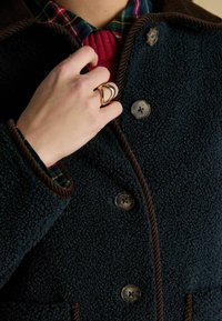 Cappotto in pile navy con dettagli in velluto a coste marrone. Presenta quattro grandi bottoni e una camicia a quadri multicolore sotto, che mette in mostra un tessuto testurizzato.