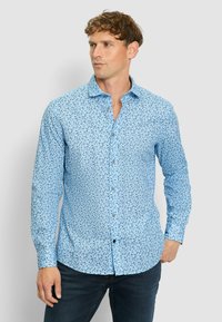 Himmelblaues Button-Down-Hemd mit floralem Muster, langen Ärmeln und klassischem Kragen, kombiniert mit dunklen Jeans.