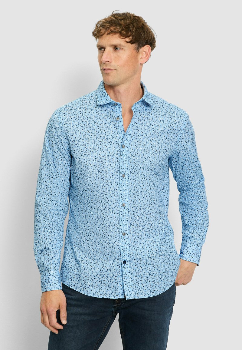 Himmelblaues Button-Down-Hemd mit floralem Muster, langen Ärmeln und klassischem Kragen, kombiniert mit dunklen Jeans.