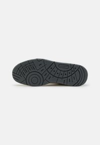 Semelle de chaussure en caoutchouc noir avec des rainures à motifs et le logo Lacoste embossé près du centre.