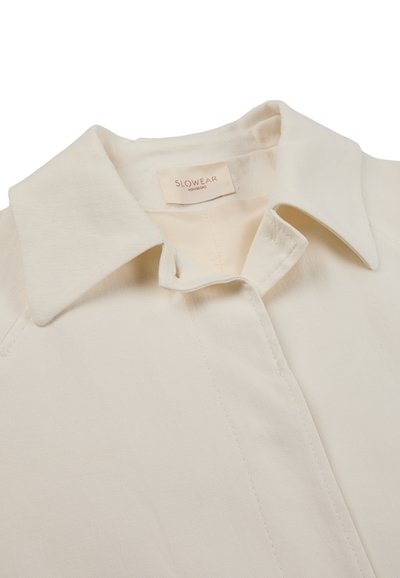 Camicia color crema con collo, patta di bottoni nascosta ed etichetta "SLOWEAR MONTEDORO" all’interno dello scollo.