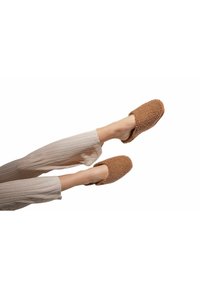 Brown fuzzy slippers with a soft texture, open back design, and rounded toe. Paired with light beige ribbed pants.