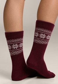 Bordowe skarpetki wykonane na drutach, ozdobione białym płatkiem śniegu i geometrycznym wzorem na mankiecie. Miękka faktura i wygodne dopasowanie.