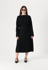 Musta neulemekko pitkillä hihoilla, ribbikuviointi ja levenevä hameosa. Yhdistettynä aurinkolaseihin ja mustiin korkokenkiin.