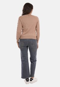 Maglione beige lavorato a maglia con dettagli a coste, indossato con jeans blu a vita alta e sneakers bianche. Texture liscia e design aderente.