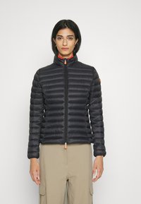 Zwarte gewatteerde jas met een hoge kraag en een voorrits, met horizontale stiksels en een oranje accent bij de rits.