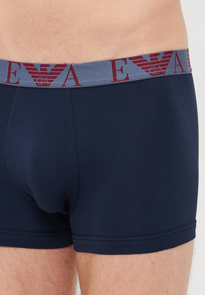 Marineblaue Baumwoll-Boxershorts mit einem grauen elastischen Bund, der mit burgunderfarbenen Logodetails versehen ist. Glatte Textur und figurbetontes Design.