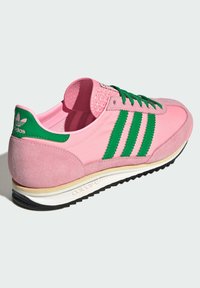 Tênis rosa com detalhes verdes, apresentando três riscas verdes, materiais em camurça e têxtil, colarinho acolchoado e sola de borracha preta.