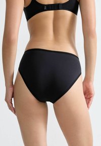 Schwarze, hoch sitzende Unterwäsche aus glattem Stoff mit welligem Saum. Einfaches Design ohne sichtbare Muster oder zusätzliche Akzente.