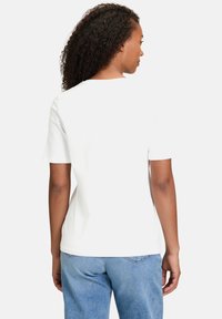 T-shirt blanc à manches courtes avec un col rond, fabriqué en coton lisse. Le dos présente un design simple sans motifs ni accents.