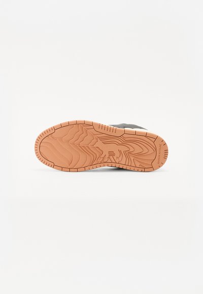 Suela de zapato con un patrón texturizado en goma marrón clara. Presenta surcos para mayor tracción y un logotipo sutil en el lado.