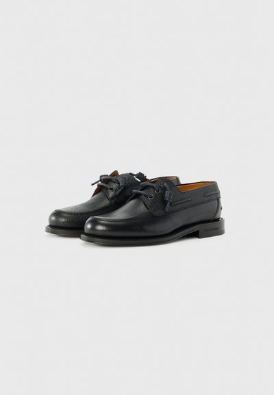Des chaussures noires en cuir avec une finition texturée, un bout rond et des lacets contrastants. Elles ont un petit talon et un détail de marque sur la semelle.