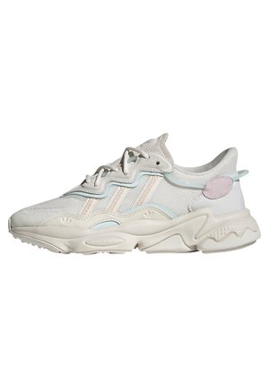 Biały i jasnoniebieski sportowy sneaker z teksturowaną podeszwą, wiązaniem z przodu, siateczkową cholewką oraz owalnym różowym akcentem w pobliżu pięty.