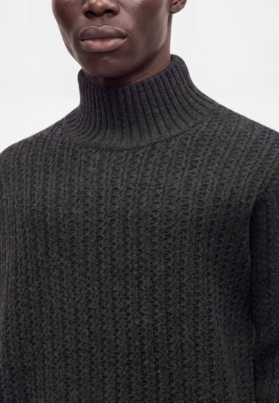 Homme portant un pull à col roulé tricoté gris foncé, montrant la texture détaillée du tissu ainsi qu'une partie du cou et du bas du visage.