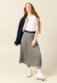 Jupe midi plissée florale en bleu marine et crème avec une taille en bleu marine, associée à un t-shirt blanc et une veste en jean, le tout complété par des baskets blanches.