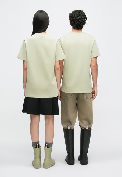 Svetlozelené tričká, voľný strih, skombinované s čiernou sukňou a béžovými nohavicami. Obuv zahŕňa zelené čižmy a čierne gumáky.