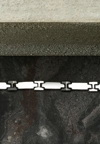 Catena metallica con anelli bianchi e neri alternati, posizionata su una superficie scura e testurizzata con un bordo grigio chiaro sullo sfondo.