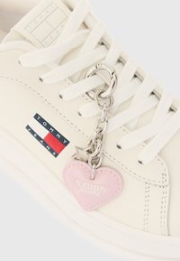 Λευκόsα sneaker Tommy Jeans με λευκά κορδόνια, λογότυπο στο πλάι και μια ασημένια αλυσίδα με ροζ καρδιά και αστέρι κρεμασμένα.