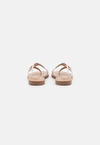 Flate sandaler laget av lys tan-lær, med flere tynne stropper som krysser over foten, med en glatt innersåle og et minimalistisk design.