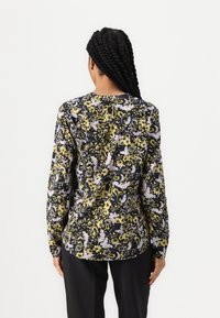 Langermet bluse med svart bakgrunn, med et blomstermønster i gult og lavendel. Glatt tekstur, rundet hem, og tettsittende passform.