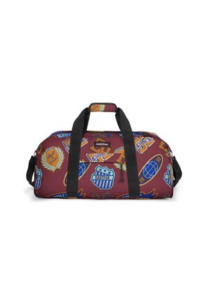 Duffle bag in maroon fabric, featuring colorful patches and logos. Durable black handles and a zipper closure. Rectangular shape.