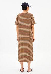 Brown striped maxi dress with short sleeves, soft fabric, crew neck, and a relaxed fit. Worn with black sandals and a navy cap.