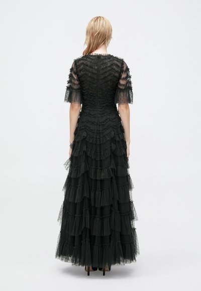 Czarna wieczorowa suknia z warstwowymi falbanami, przezroczystymi krótkimi rękawami, teksturowanym korpusem i długością do ziemi. Zamek błyskawiczny z tyłu.