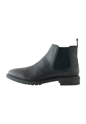 Botín chelsea de cuero negro con paneles laterales de malla elástica, acabado texturizado, punta redondeada y suela de goma duradera con un ligero tacón.