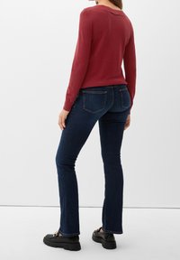 Rode lange mouwen trui met een ronde hals, gecombineerd met donkerblauwe jeans. Zwarte platform schoenen met decoratieve hardware-details.