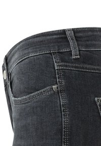 Los jeans de mezclilla negra presentan un diseño ajustado con costuras visibles, dos bolsillos traseros y acentos de hardware metálico cerca de los bolsillos.