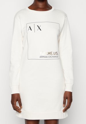 Person wearing a white long-sleeve dress with "A | X" and "YOU. ME. US. ARMANI EXCHANGE" printed inside a square on the chest.