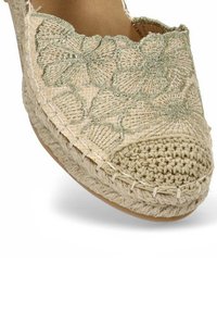 Espadrille beige con patrón floral bordado, punta redonda trenzada, parte superior de yute texturizado y plantilla suave parcialmente visible.