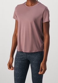 Cienka fioletowa koszula z krótkim rękawem w dopasowanym kroju, zestawiona z czarnymi legginsami o wysokim stanie z ciemnoszarym wzorem przypominającym kamyki.