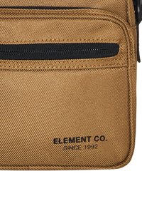 Beige Stoffbeutel mit strukturiertem Oberflächen, ausgestattet mit einem schwarzen Reißverschluss und dem eingeprägten Logo "ELEMENT CO." auf der Vorderseite. Kompakte rechteckige Form.