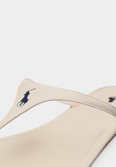 Πέδιλο με μπεζ λουράκια σε στυλ στρινγκ, με ραμμένες λουρίδες που φέρουν το μαύρο λογότυπο παίκτη πόλο στον επάνω ιμάντα και στη σόλα.