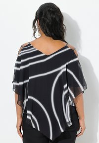 Blusa a righe in bianco e nero realizzata in tessuto trasparente, con scollo a V, spalle scoperte e orlo asimmetrico fluente. Dettagli in hardware argentato.
