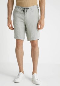 Jasnoszare lniane szorty o luźnym kroju, z elastycznym paskiem ze sznurkiem i podwiniętymi nogawkami. W zestawieniu z białymi trampkami dla uzyskania neutralnego wyglądu.