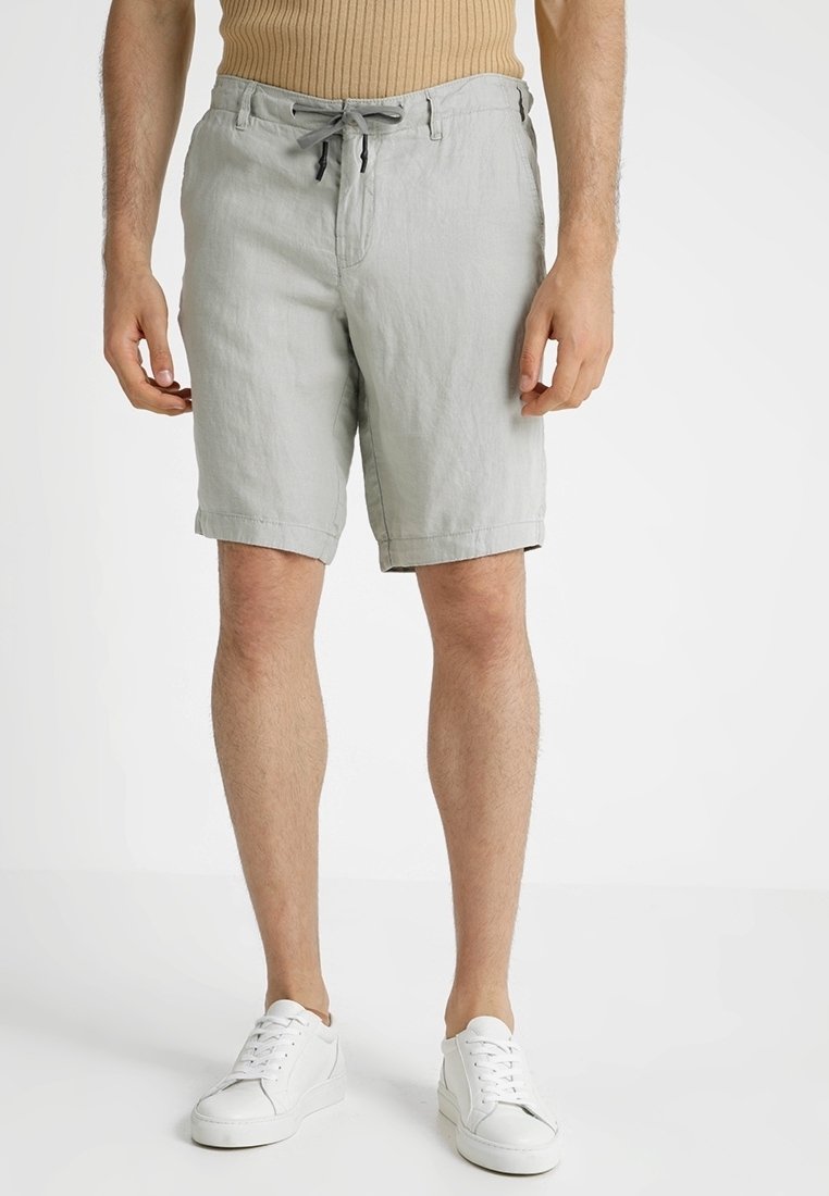 Jasnoszare lniane szorty o luźnym kroju, z elastycznym paskiem ze sznurkiem i podwiniętymi nogawkami. W zestawieniu z białymi trampkami dla uzyskania neutralnego wyglądu.