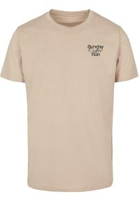 Beige cotton T-shirt with short sleeves and round neckline. Features black "Sunday Coffee Run" text design on the chest. Smooth texture.