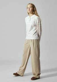 Polo shirt a righe rosa chiaro con colletto, abbinato a pantaloni beige plissettati e scarpe slip-on marroni. Tessuto liscio, vestibilità rilassata.
