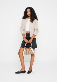 Cardigã de malha bege claro sobre um top cropped branco, combinado com uma saia de ganga preta. Segurando uma bolsa multicolorida e usando sapatos pretos planos.