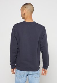 Donkerblauwe ronde hals sweatshirts, gestructureerde stof, ribgebreide manchetten en zoom, ontspannen pasvorm, zichtbare stikseldetails op de achterkant.