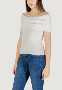 Top bianco a coste con scollo off-the-shoulder e maniche corte, caratterizzato da un corpo testurizzato e design aderente, abbinato a jeans in denim blu.